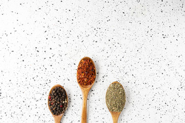 Collection of three spices on wooden spoons on white cement background