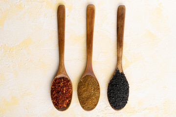 Collection of three spices on wooden spoons on yellow cement background