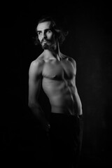 Fototapeta na wymiar Portrait of a handsome young man with a naked torso. A man with curly hair and a beard. Black and white photo. Muscle, fitness, dance. Body sculpture. Orientation.