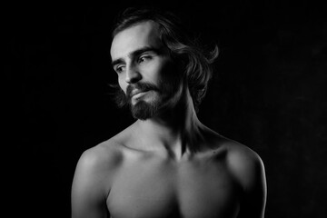 Obraz na płótnie Canvas Portrait of a handsome young man with a naked torso. A man with curly hair and a beard. Black and white photo. Muscle, fitness, dance. Body sculpture. Orientation.