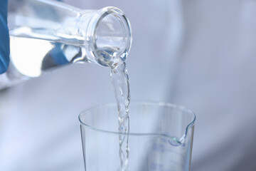 Pure water is poured from a bottle into transparent glass