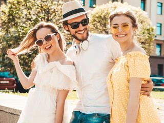 Group of young three stylish friends posing in the street. Fashion man and two cute female dressed in casual summer clothes. Smiling models having fun in sunglasses.Cheerful women and guy outdoors