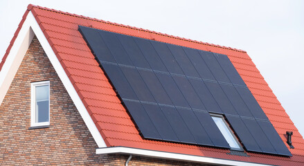 Solar panels mounted on the roof of a modern new-build house with red roof tiles in Lemmer, Friesland, the Netherlands with blue sky. Renewable energy