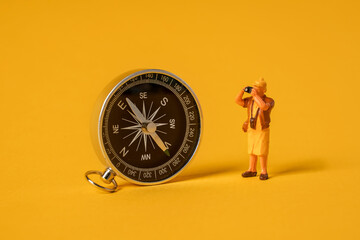 Miniature people on a yellow background, a tourist standing near a compass, travel concept