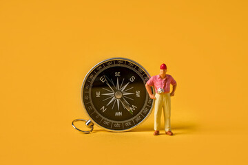 Miniature people on a yellow background, a tourist standing near a compass, travel concept