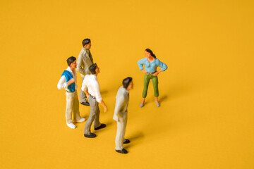 Miniature people on a yellow background, men against women at work. The concept of gender equality, feminism