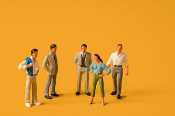 Miniature people on a yellow background, men against women at work. The concept of gender equality,...