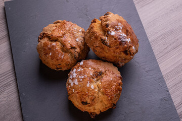 Three freshly baked fruit scones on slate plate .