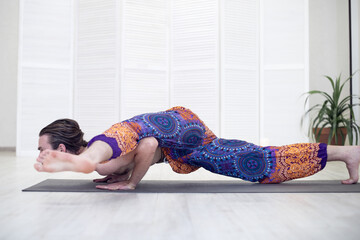 Athletic young male yogi with long hair doing yoga and Pilates in the Studio. The concept of a healthy lifestyle and natural balance.