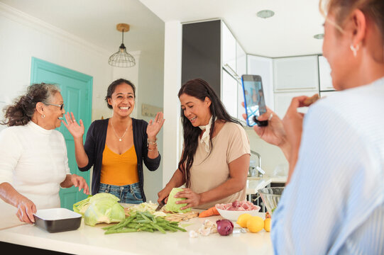 Filipino family cooking together at home - Girl taking a video of her grandmother and mother showing a recipe to her sister - Family of four women spending quality time together
