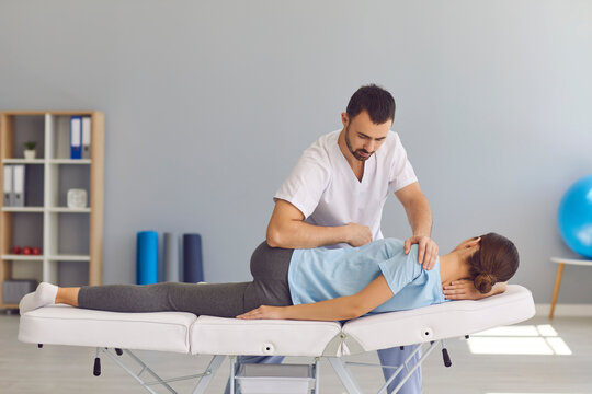 Confident man doctor chiropractor or osteopath fixing womans back and legs joints