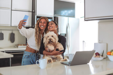 Two friends taking a selfie with the smart phone while having coffee together in the kitchen at home - 422830255