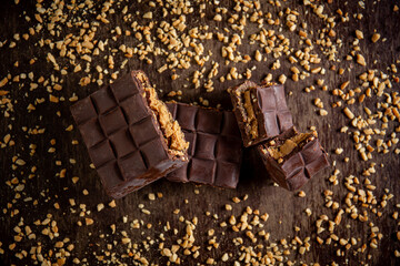 Broken assorted chocolate bar with carrot cake filling with cashew nuts around on a wooden table. Gourmet. Top view.