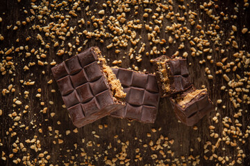 Broken assorted chocolate bar with carrot cake filling with cashew nuts around on a wooden table. Gourmet. Top view.