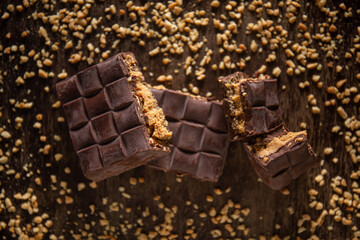 Broken assorted chocolate bar with carrot cake filling with cashew nuts around on a wooden table. Gourmet. Top view.