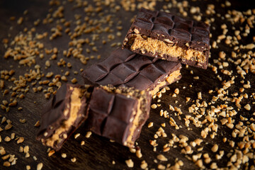 Broken assorted chocolate bar with carrot cake filling with cashew nuts around on a wooden table. Gourmet. Close up.