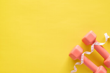 Dumbbells and measuring tape on yellow background. Fitness, sport and workout