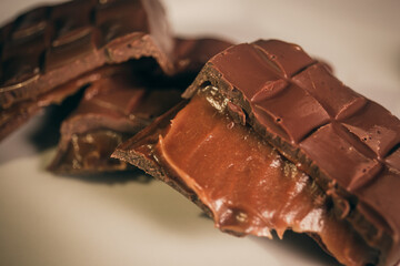 Broken assorted chocolate bar with caramel filling on a white plate. Gluten free. Close up....