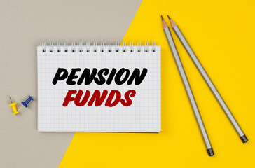 On a yellow-gray background are pencils, buttons and a notebook in which it is written - PENSION FUNDS