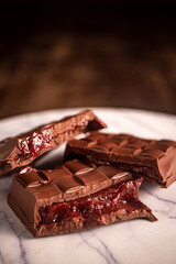 Broken chocolate bar with strawberry jam filling on a marble board. Gourmet. Close up. Space for text.