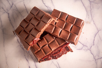 Broken chocolate bar with strawberry jam filling on a marble board. Gourmet. Close up. Top view.
