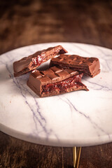Broken chocolate bar with strawberry jam filling on a marble board. Gourmet. Close up.