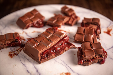 Broken chocolate bar with strawberry jam filling scattered on a marble board. Gourmet.