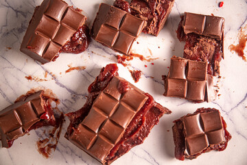 Broken chocolate bar with strawberry jam filling scattered on a marble board. Gourmet. Top view.