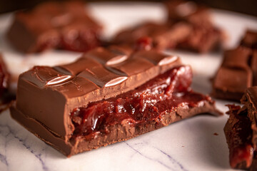 Broken chocolate bar with strawberry jam filling scattered on a marble board. Gourmet.