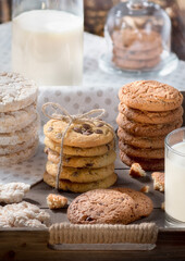 Homemade oatmeal and chocolate chip cookies in rustic wooden tray, glass of milk, bottle, cozy early breakfast concept