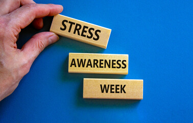Stress awareness week symbol. Wooden blocks with words 'Stress awareness week'. Beautiful blue background. Doctor hand. Psychological, business and stress awareness week concept. Copy space.