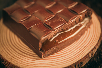 Tasty broken chocolate bar with passion fruit filling on a tree trunk on a wooden table. Close up. Selective focus. 