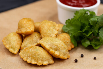 Small chebureks on craft paper close-up. Served with ketchup and herbs.