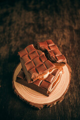 Tasty broken chocolate bar with passion fruit filling on a tree trunk on a wooden table. Close up. Selective focus. Space for text.