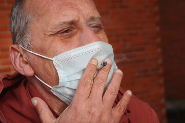 Мan smokes a cigarette through a medical mask. Сoncept of harm to health caused by smoking,...