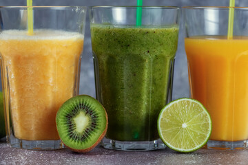 Three glasses in a row with orange juice and banana orange kiwi smoothie