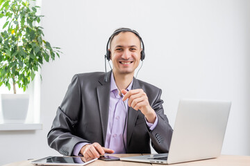 Man working in the office from dawn to dusk. Communication via the Internet. Young businessman using tablet laptop and headphones phone connecting wi-fi. Sunset light. Negotiations on line.