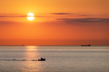 Sunset in the ocean with large sun dusk in orange sky and ships and boats silhouettes. Sea sunrise...