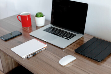 Office at home. Laptop, notebook, pen are on the table near the white wall.