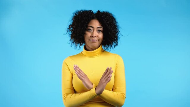 Mixed race woman disapproving with no crossing hands sign make basta, negation, enough gesture. Denying, Rejecting, Disagree, Portrait of pretty lady on blue background