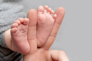The father is holding the feet of the newborn baby. grey colour. tenderness. Father's day concept.