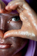A girl with purple hair and glowing skin. An alien or a fairy with glowing skin. Her hands are folded in front of her face in a heart shape