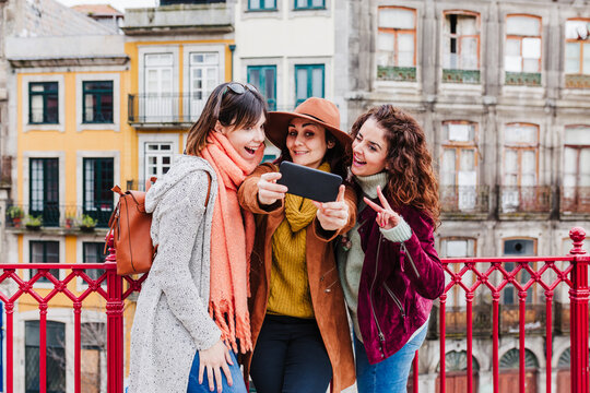 three women sightseeing Porto views and taking picture with mobile phone. Travel and friendship concept
