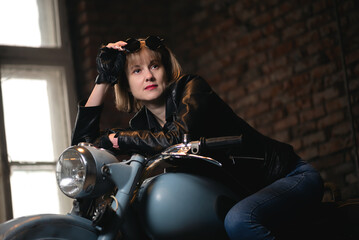 Fototapeta na wymiar Young biker woman is sitting on the retro motorbike in the old garage.