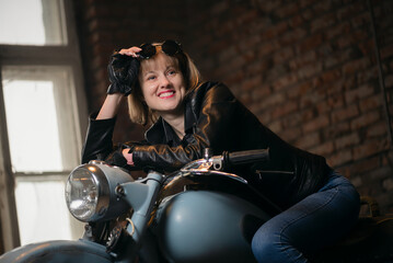 Fototapeta na wymiar Happy young motorbiker woman is sitting on the retro motorbike in the old garage.