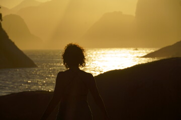 girl in silhouette enjoying a beautiful sunset on the beach of Piratininga, Niter&oacute;i, overlooking the hills of Rio de Janeiro. Sunny summer day.