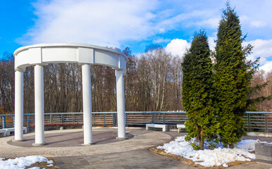 White columns in the form of a rotunda on the shore of a reservoir in early spring in sunny weather