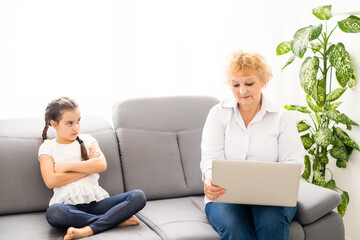 Mature grandmother helping child with homework at home. Satisfied old grandma helping her granddaughter studying in living room. Little girl writing on notebook with senior teacher sitting next to her