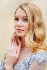 Portrait of a young blonde woman in a delicate blue dress against a beige wall. Blonde girl, makeup and hairstyle