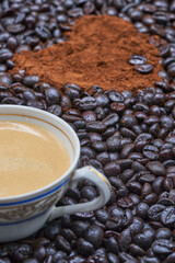 Cup with coffee with milk on roasted coffee beans and ground coffee with a heart shape.